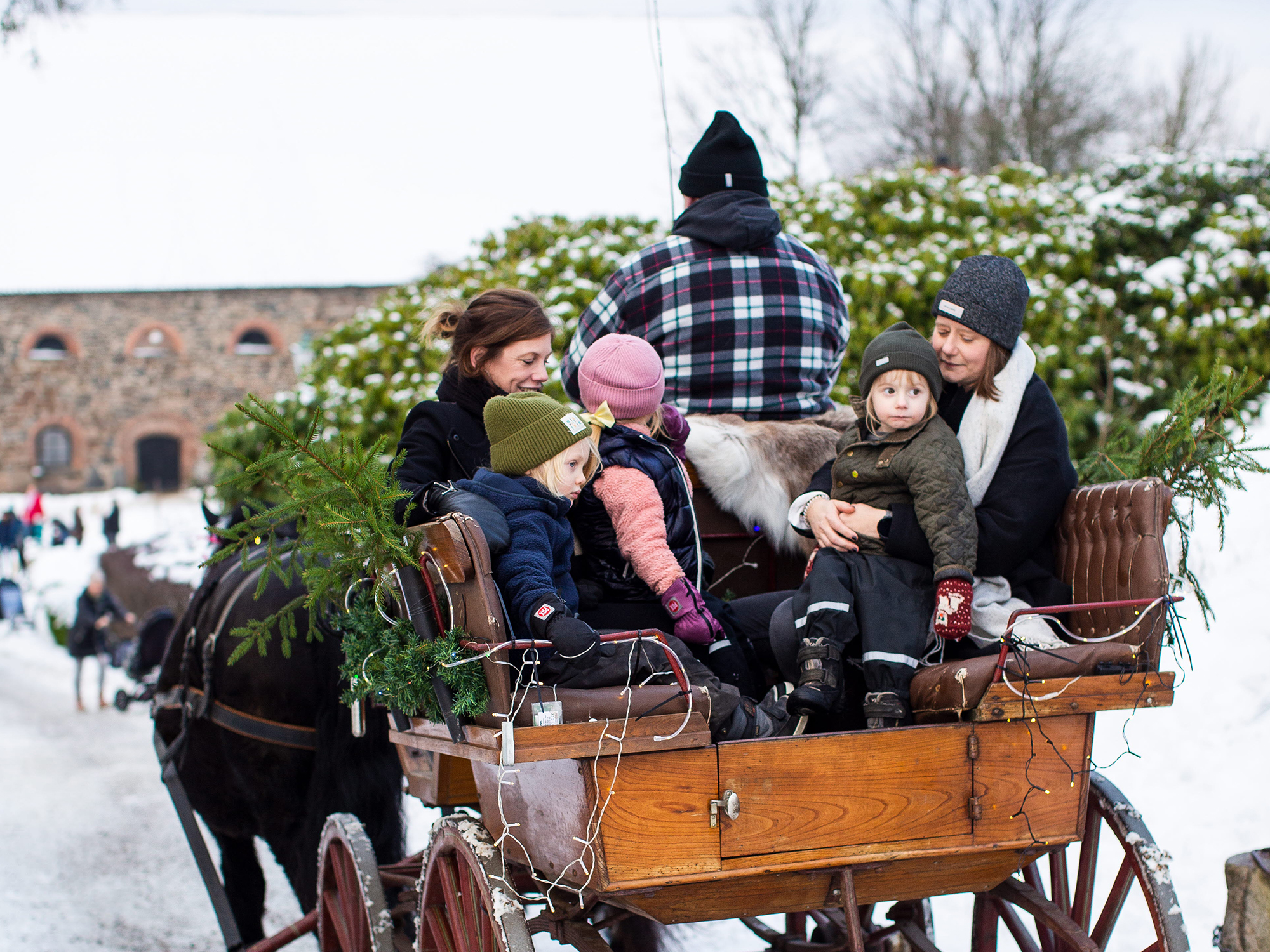 Två vuxna och två barn åker häst och vagn i en julig slottsmijö.