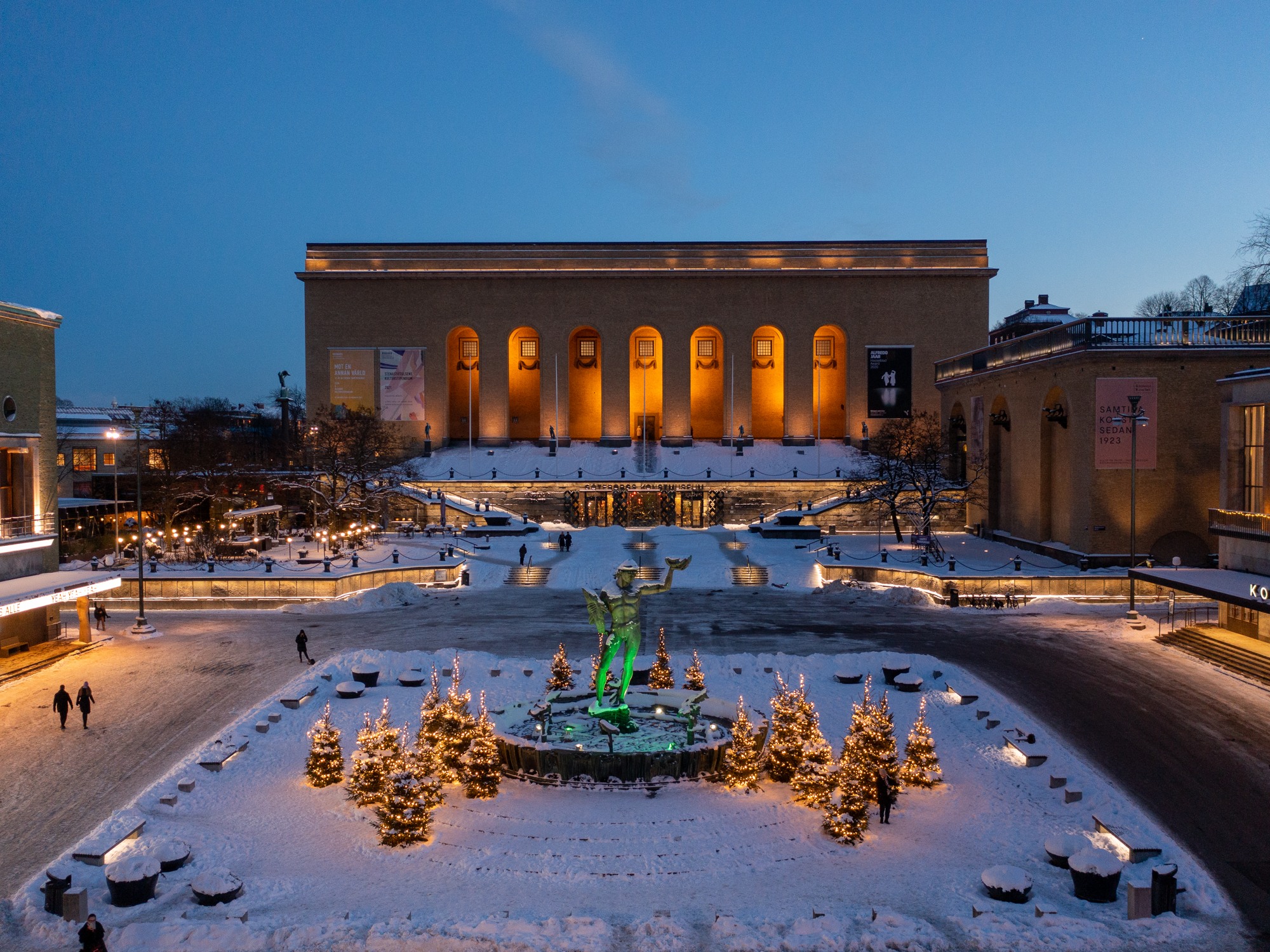 View of a snowy square with the statue of Poseidon in the middle, surrounded by lit pine trees, and the Göteborgs konsthall - the centre for contemporary art in Gothenburg - in the background.