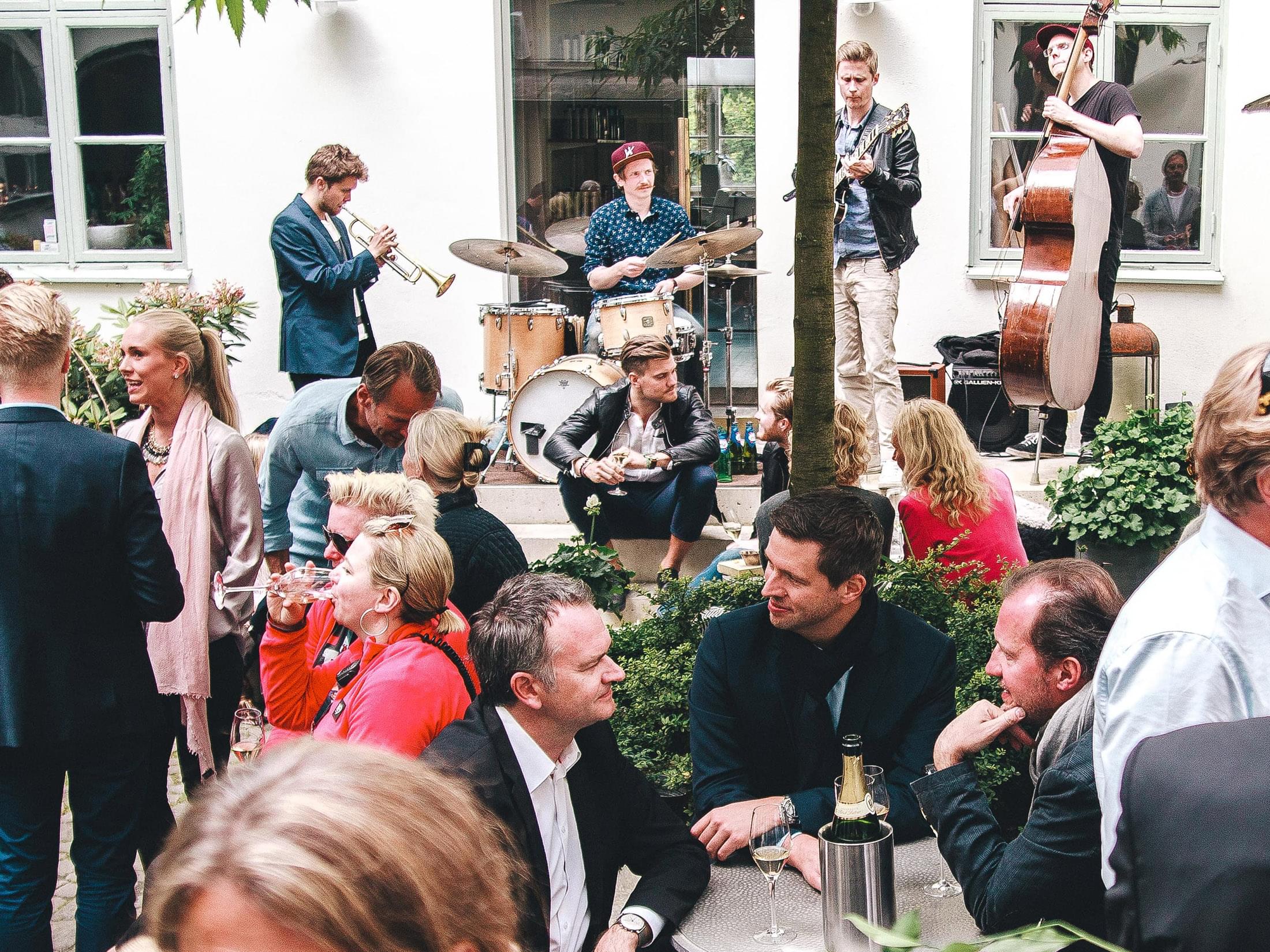 Folk minglar och dricker öl på innergård där ett jazzband spelar.