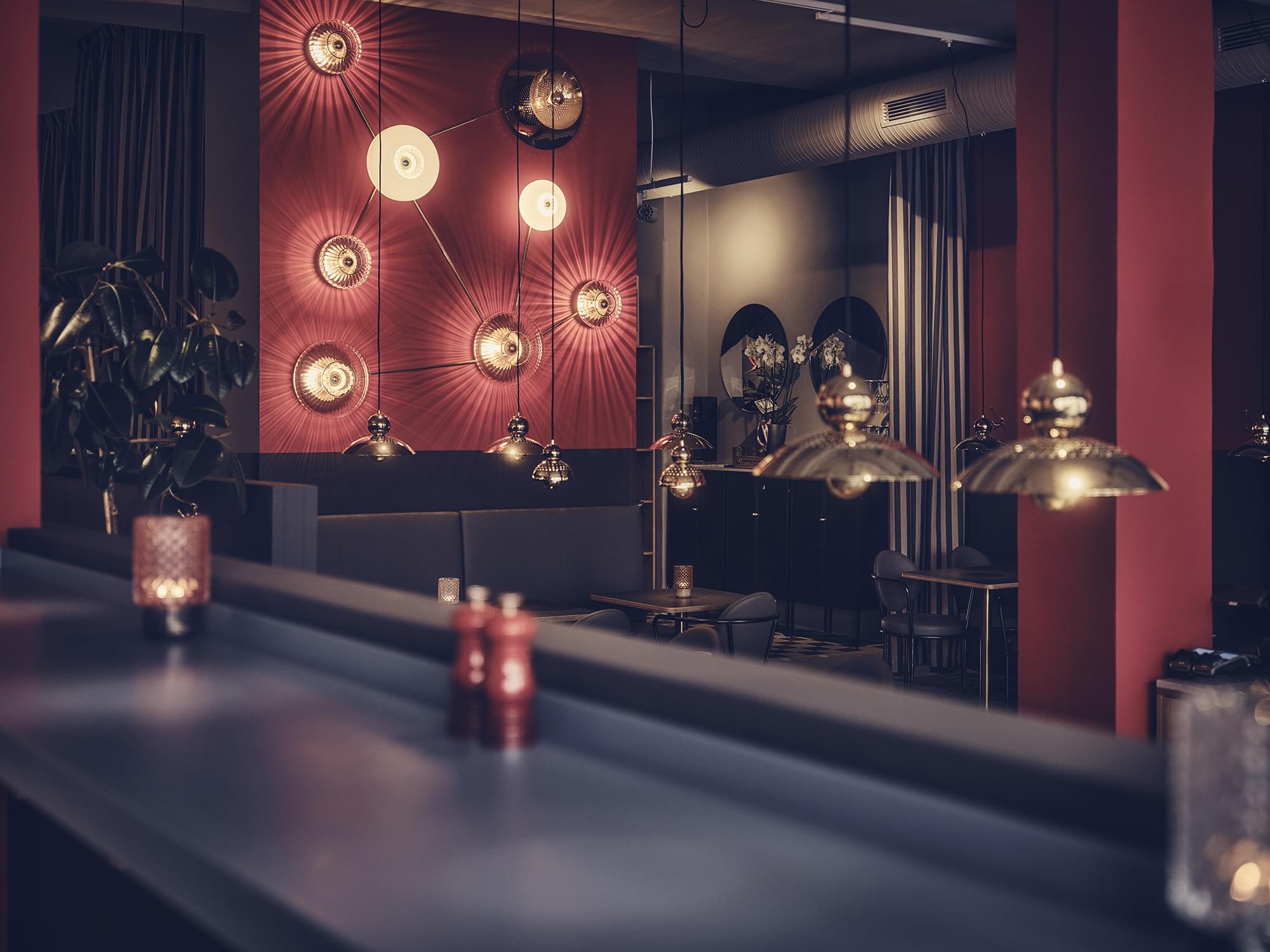 Bild tagen från bardisk ut mot restaurangen, guldfärgade lampor hänger mot en röd bakgrund.