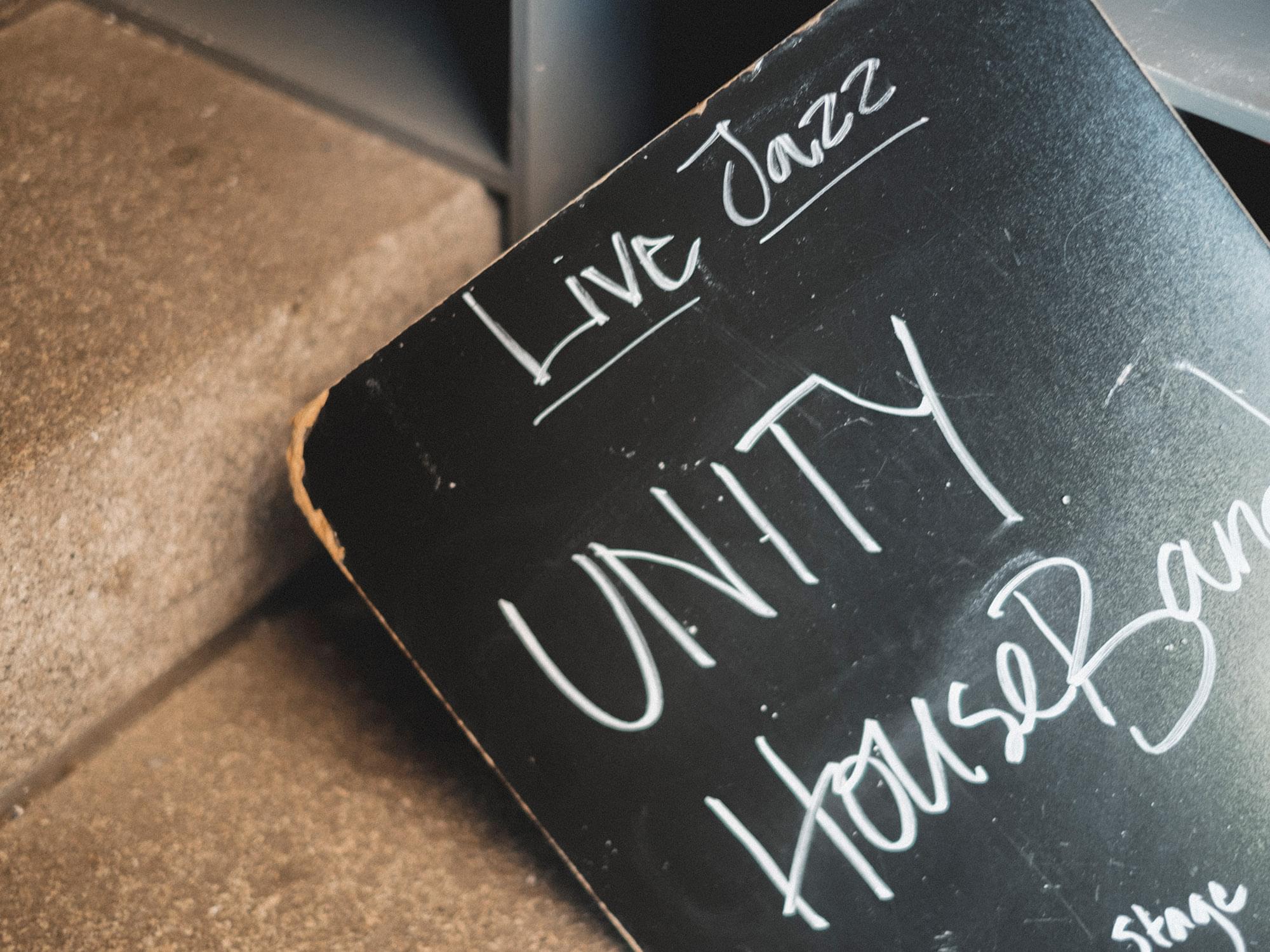 En svart tavla med texten "Live Jazz" och "Unity House Band" .
