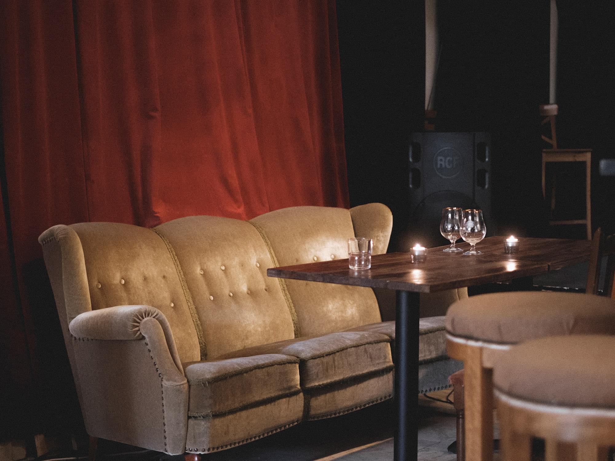En soffa står mot en röd gardin, framför står ett bord med två tomma ölglas.