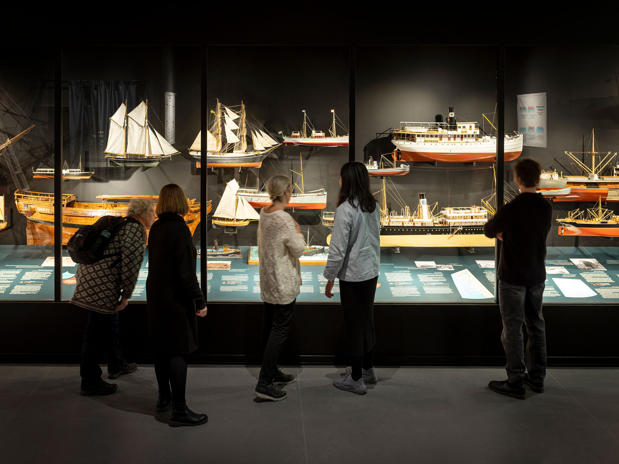 Fem vuxna personer tittar på en utställning med fartygsmodeller.