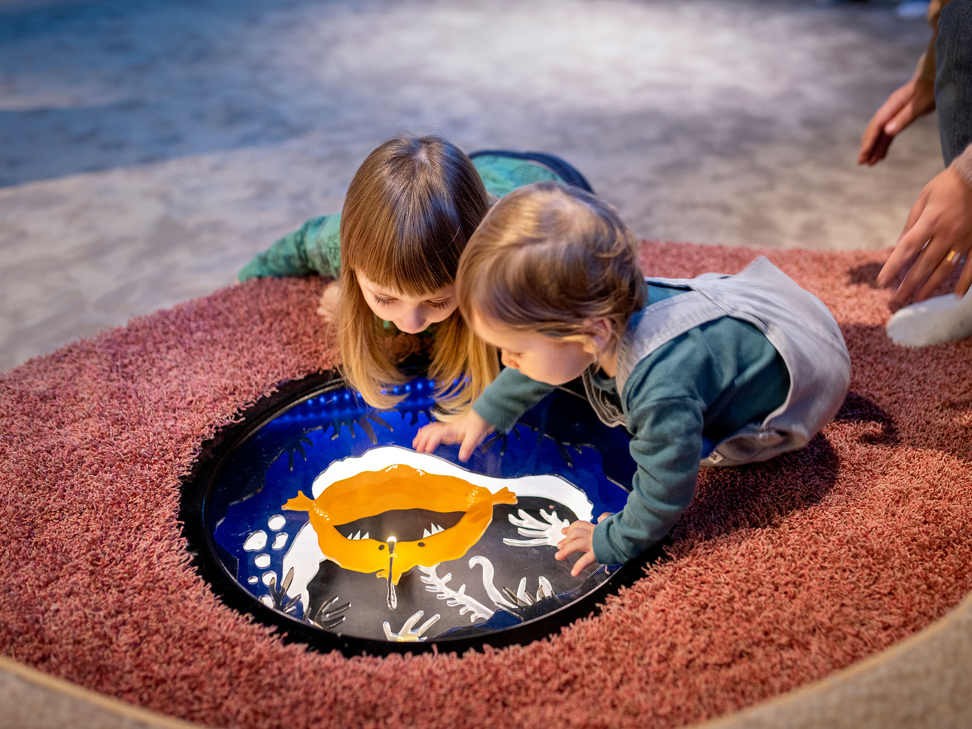 Två små barn tittar på en bild på en fisk, liggandes på en mjuk matta.