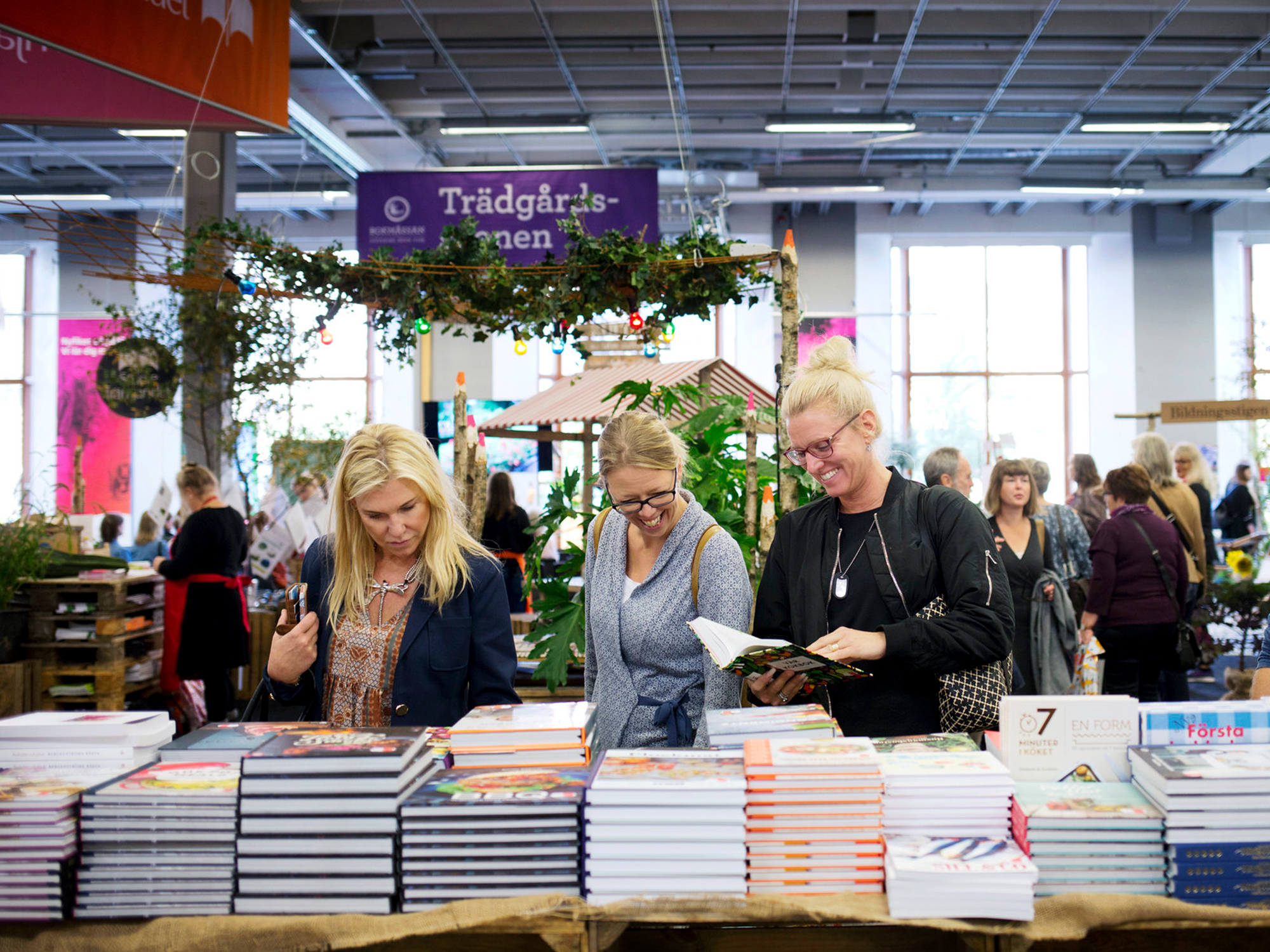 Tre personer står vid ett bod med staplar av böcker på bokmässan i Göteborg.