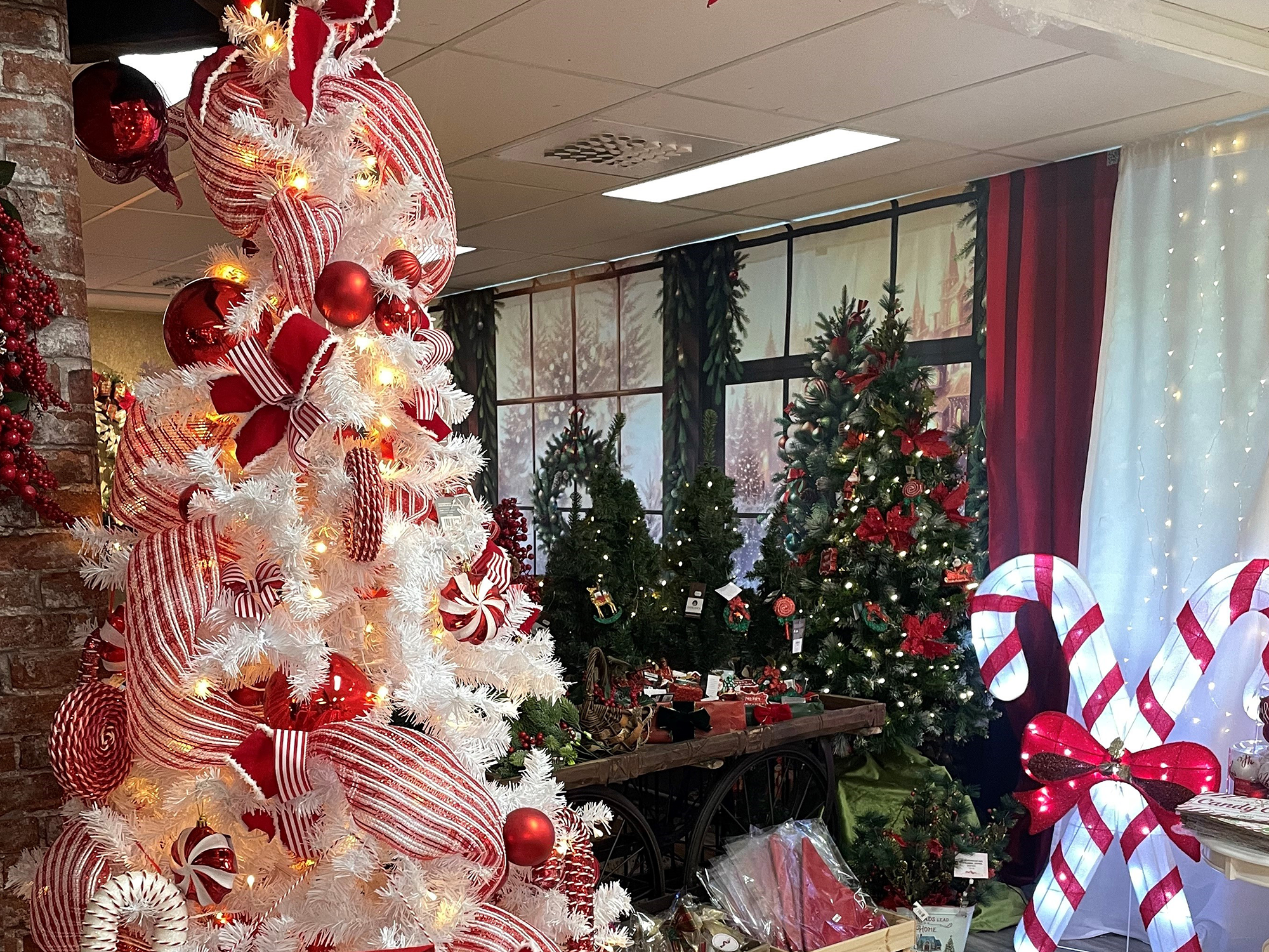 Julbutik med en stor vit julgran fylld med röda utsmyckningar, en tomte, två polkagrisar, bland andra juliga dekorationsbitar