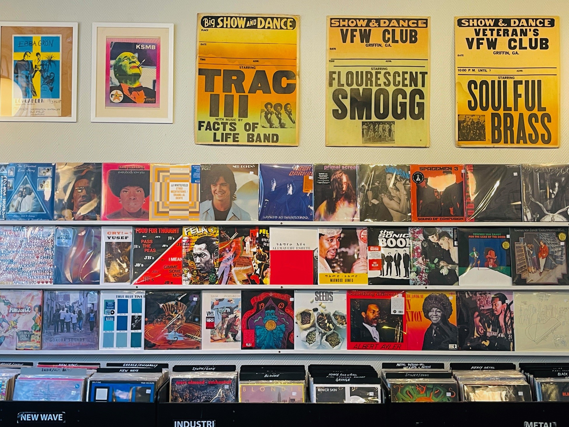 Different vinyl records and some posters hanging on a wall.