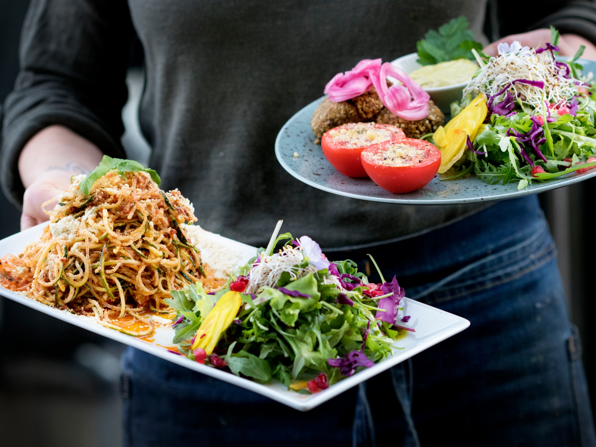 En person håller i två tallrikar med veganska maträtter.